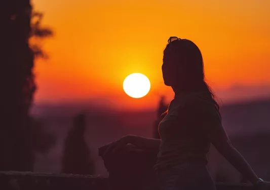 Woman backlit in front of vibrant sunset horizon.