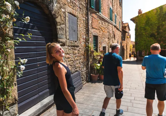 Three guests walking down brick road, one smiling at camera amidst storefronts.