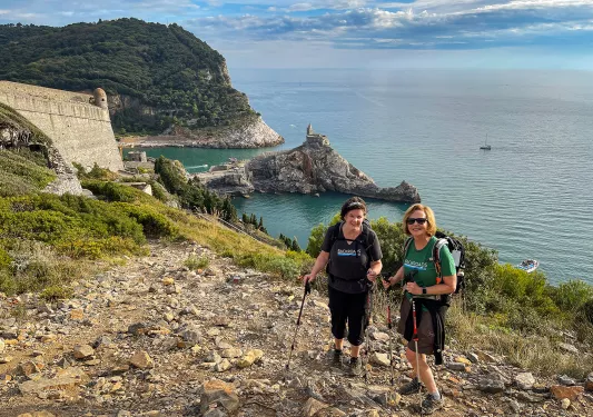 Two guests on rocky cliffside, Chiesa di San Pietro in distance.