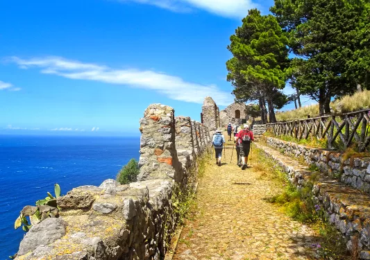 Guests walking next to ocean cliffside, towards small sandstone building.