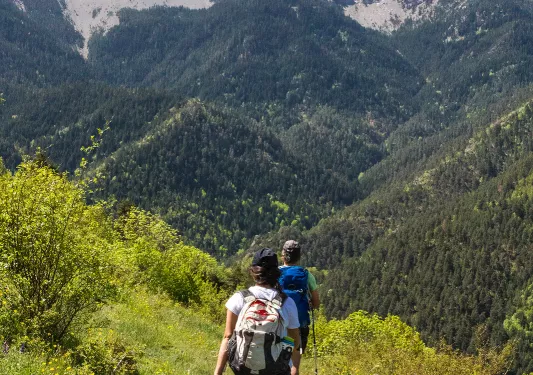 Two guests on mountain trail, walking towards large range.