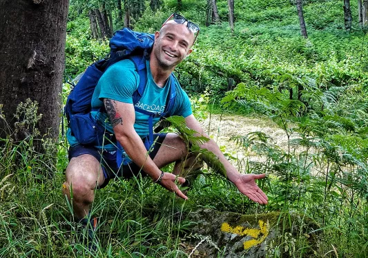 Guest in bushes off trail, gesturing to mossy rock.