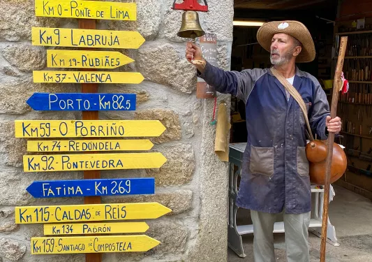 Local in hiking gear ringing bell, assortment of direction signs to his right.