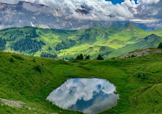 Wide shot of green, hilly, mountainous vista, small pool in foreground.
