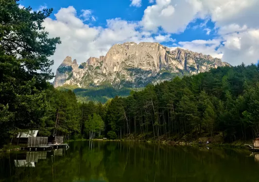 Shot of a small lake. Large, cloud-tipped mountain range in background.