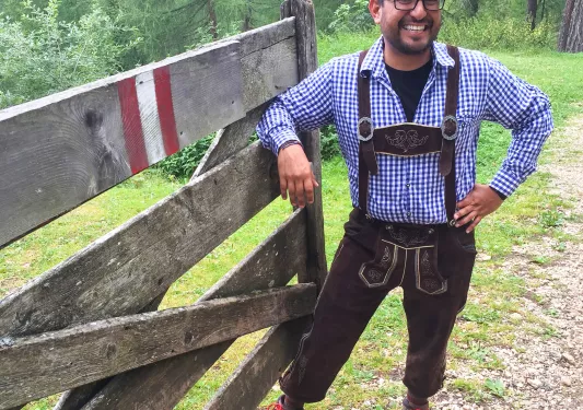 Local guide in traditional clothing posing for camera, leaning on wooden fence.
