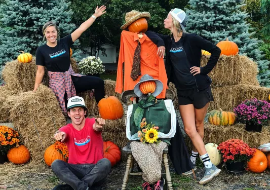 Three guests posing with pumpkin-headed scarecrows.