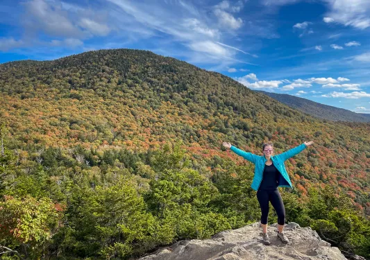 Guest gesturing to vast forest landscape, arms outstretched. 