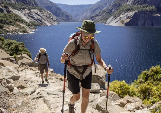 Two guests hiking beside large body of water.