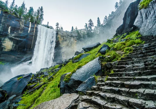 Wide shot of waterfall, rocky stairway in foreground.