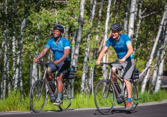 Two guests cycling, forest in background.