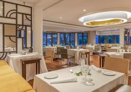 Dining hall with a large circular light in the ceiling, and wine glasses on each table