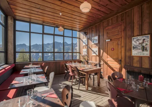 Dining area in a wooden-lodge room with large windows looking out to the mountains