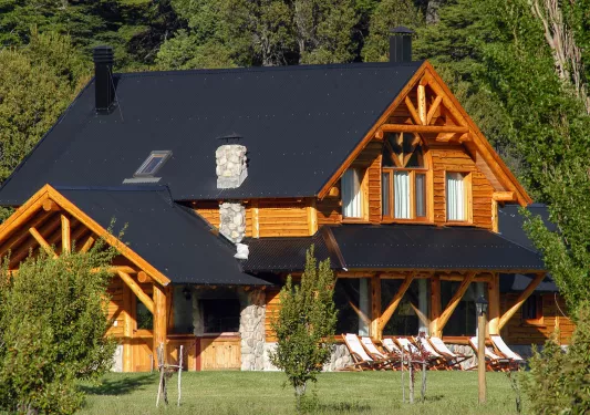 Exterior view of a wooden log cabin with a black roof and a stone chimney