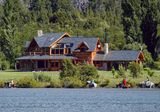Wide exterior view of a wooden log cabin with a lake in front