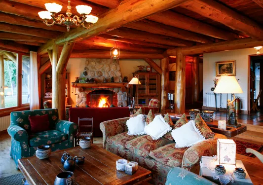 Indoor lodge of a wooden log cabin with a stone fireplace and sofas surrounding a coffee table