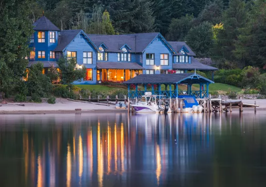 Blue lodge building with a large lake in front with boats docked by a pier