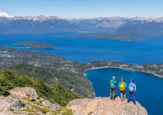 Group of 3 people standing on a cliff, looking out to a lake