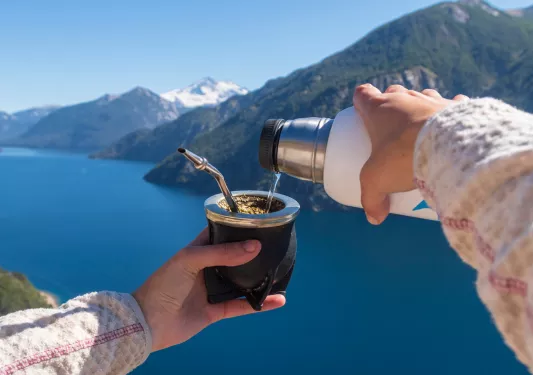 Hand pouring water into a mate, with a large lake in the background