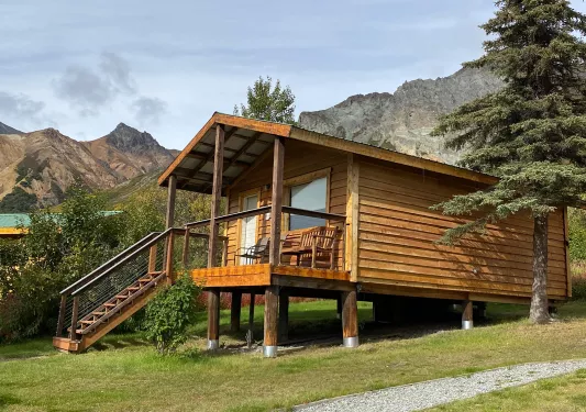 Wooden cabin with a small staircase in front and wooden chairs on the porch