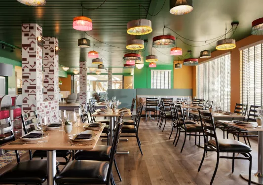 Indoor dining area with black chairs and wooden tables, with colorful light fixtures