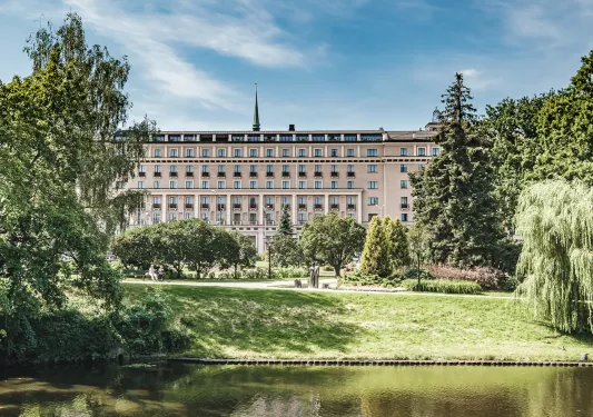 Large building with 4 stories of windows with an outdoor grass area and a small pond