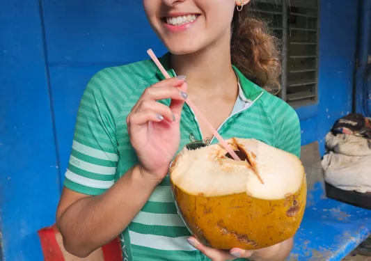 Woman holding up an opened coconut with a straw coming out of it