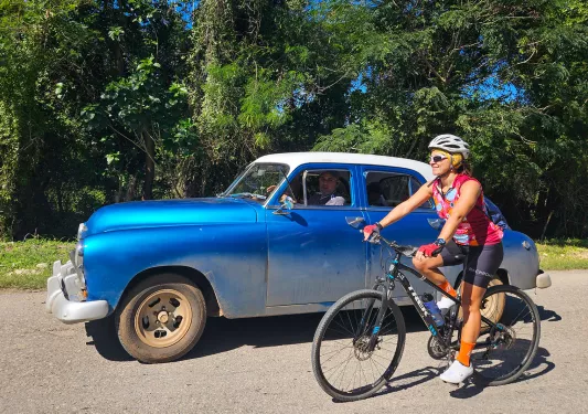 Woman riding a bike next to a blue car from the 1960s