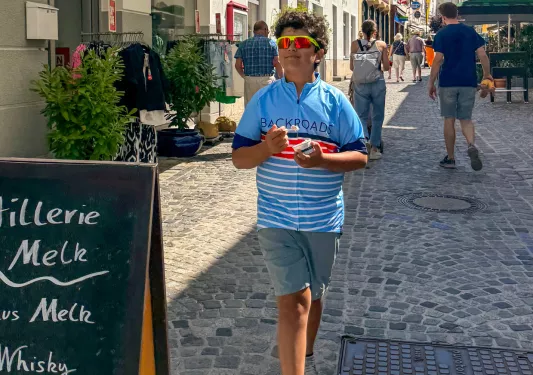 Boy wearing sunglasses, walking on a stone pathway in a town center
