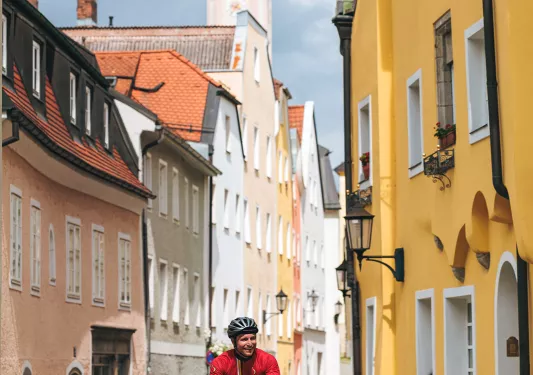 Man in red biking in a town, surrounded by red and yellow buildings