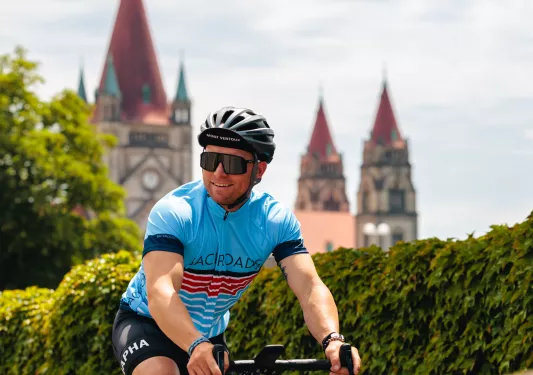 Man riding a bike and wearing sunglasses, with a clock tower in the distance