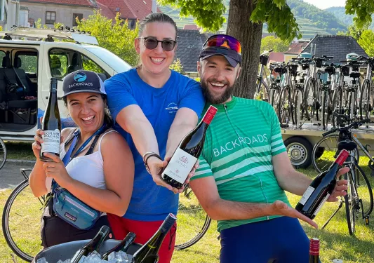 Two women and one man holding bottles of wine