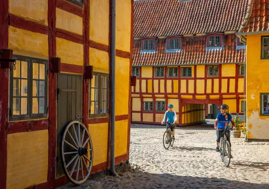 Two bikers biking through corridors of red and yellow buildings