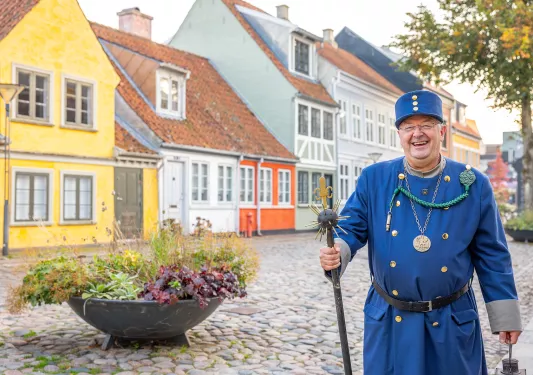 Police in blue guard suit, in front of yellow and red brick houses