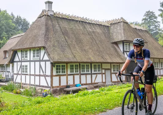 Man biking in front of a white hut-style building in a grass field