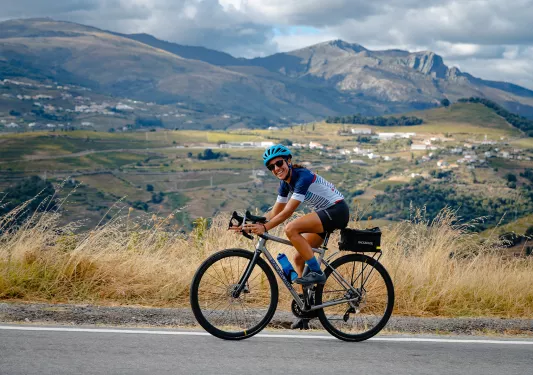 Woman smiling while biking on an asphalt road, with a large valley in the background