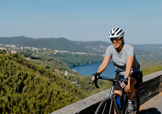 Woman smiling and riding a bike on a stone bridge with a valley in the background