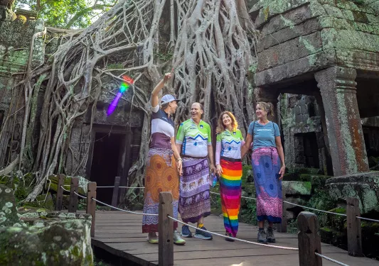 Four people in dresses walk through a forest