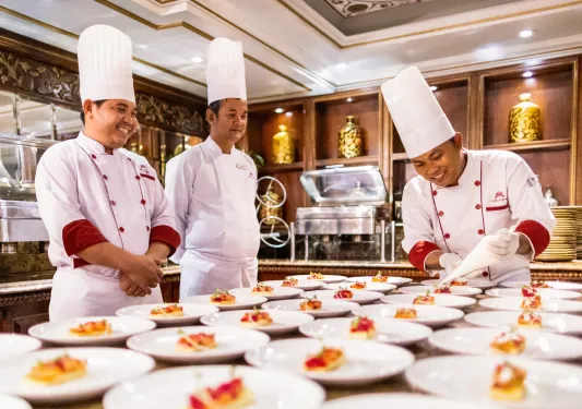 Three chefs smiling while decorating a table full of plates