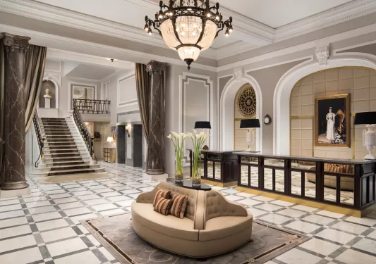 Hotel lobby with a staircase on the left and a brown, cushioned chair in the center