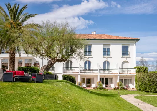 Exterior view of a white building with a grass hill in front