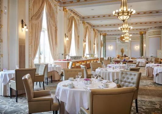 Indoor dining hall with tan, cushioned seats and tables with white cloths over