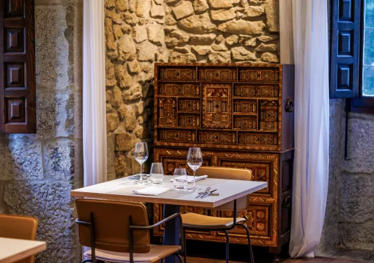 Stone-walled dining room with multiple chairs and tables, with wine glasses on each table