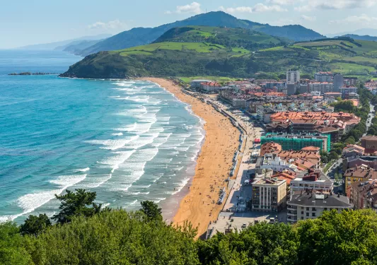 Sky view of a small town next to a beach, with grassy hills in the distance