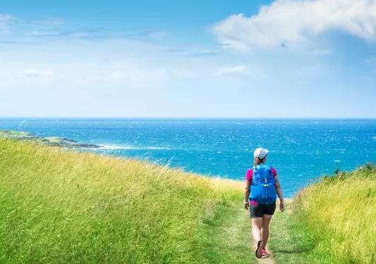 Woman hiking in a grassy field, with the ocean in the distance
