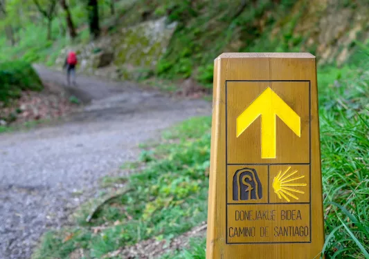 Hiking sign on a trail, with a person walking on a gravel path