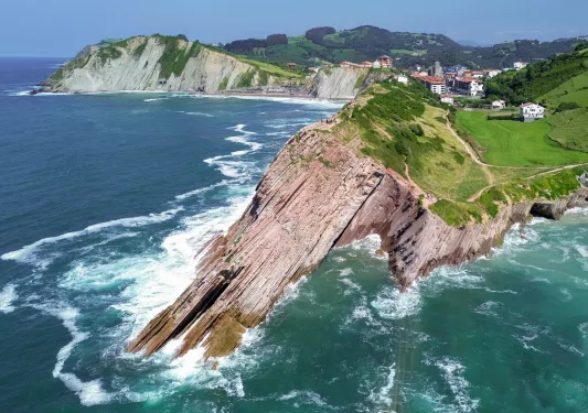 Slanted cliff on the coast of an ocean, with a small town in the distance