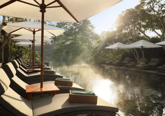 Outdoor pool surrounded by reclining chairs, white smoke on the water