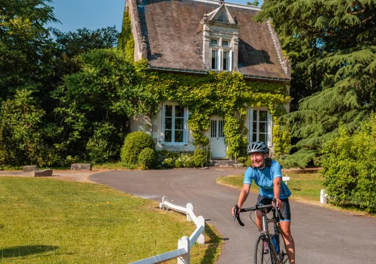 Woman riding a bike in front of a rustic, cottage-style building on an asphalt road