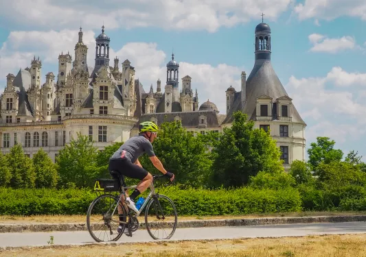 Man biking on an asphalt road, with a rustic, castle-like building in the background